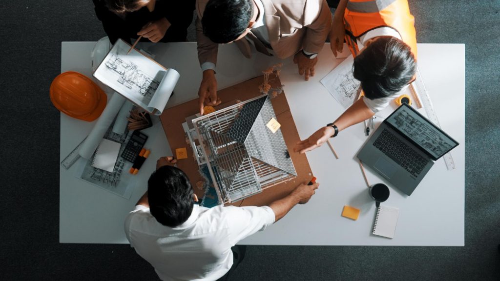 Equipe de engenharia analisando maquete e projeto com laptop aberto em software licenciado