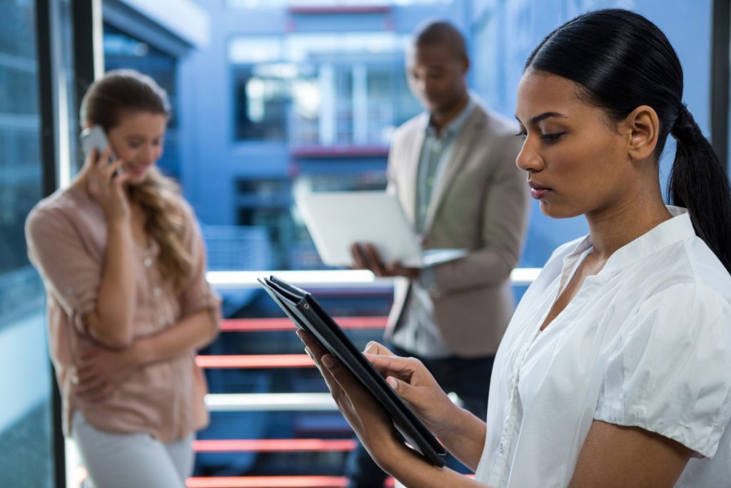 Profissionais usando celular, notebook e tablet em ambiente corporativo moderno